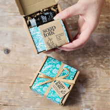 Load image into Gallery viewer, Hand holding a box of Soap Folk products on a wooden surface