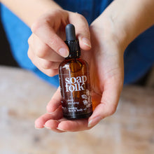 Load image into Gallery viewer, Person holding a bottle of Soap Folk oil with a blurred background