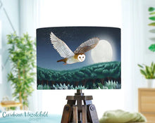 Load image into Gallery viewer, Lamp with a design of an owl flying over a moonlit landscape, placed on a stand with a blurred indoor background.