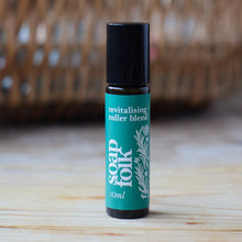 Load image into Gallery viewer, Soap Folk revitalising roller blend bottle on a wooden surface with a blurred wicker basket in the background.